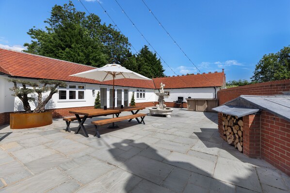Un patio con mesa y bancos de madera, una sombrilla blanca y una fuente de piedra.