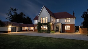 A two-story house with a red-tiled roof, multiple windows, and a well-lit front entrance.