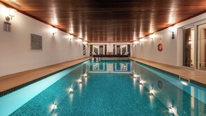 A swimming pool with a wooden ceiling and tiled floor, surrounded by walls with light fixtures and a lifebuoy.