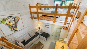 Habitación de varios niveles con cama en altillo, sofá, mesa de comedor y una mesita con una planta.