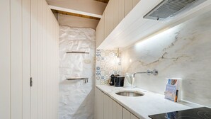 Una cocina estrecha con armarios blancos, salpicadero de mármol y placa de inducción negra.