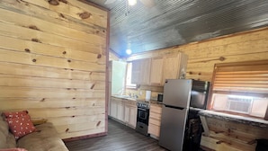 A cozy cabin-style room with a wooden floor, a sofa with cushions, a ceiling fan, and a kitchenette with a refrigerator, stove, and microwave. - Cozy cabin with AC and WiFi in delightful Murfreesboro (Murfreesboro)