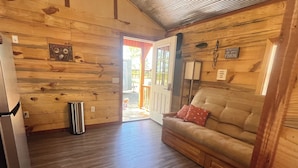 A wooden interior with a sofa, a trash can, and a door leading outside. - Cozy cabin with AC and WiFi in delightful Murfreesboro (Murfreesboro)