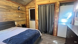 A wooden cabin bedroom with a bed, dresser, and washing machine. - Cozy cabin with AC and WiFi in delightful Murfreesboro (Murfreesboro)