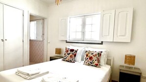 Une chambre avec un grand lit, des rideaux blancs, une fenêtre et un miroir.