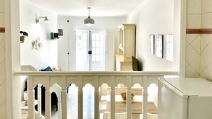 Un couloir avec une rambarde blanche, une porte donnant sur une autre pièce et un luminaire au plafond.