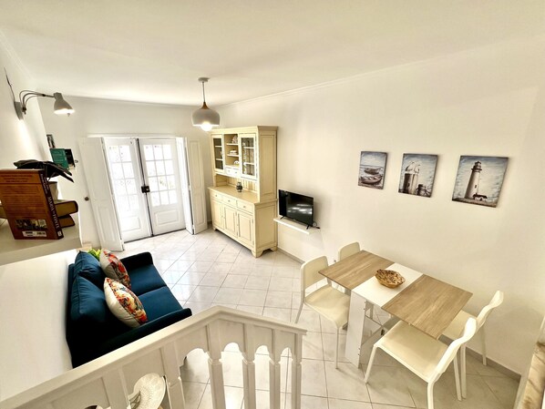 A bright, open-plan living space with a dining area, kitchen, and a staircase leading to an upper level.