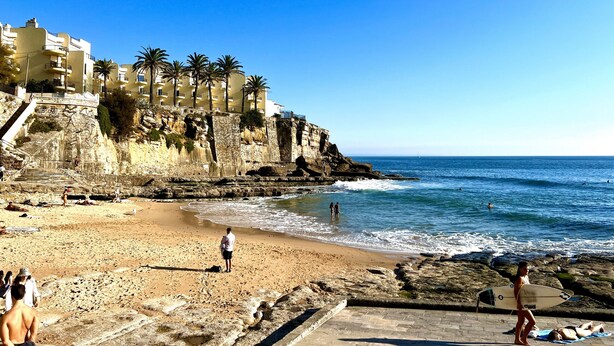 Une plage au paysage rocheux, un escalier menant à un bâtiment, et un ciel bleu dégagé.