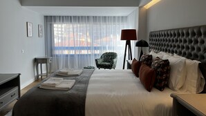 A modern hotel room with a large bed, a chair, a desk, and a window with sheer curtains. - Atrium (Cascais)