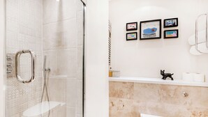 Un baño con cabina de ducha de vidrio, inodoro blanco y lavamanos con una figurita decorativa de gato.