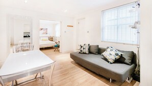 Una sala de estar moderna con un sofá gris, una mesa blanca y un gran ventanal con persianas.