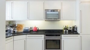 Una cocina moderna con armarios blancos, un horno de acero inoxidable, un microondas y una encimera negra.