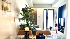 A modern living room with a glass dining table, a large potted plant, a TV mounted on the wall, and a sliding glass door leading to a balcony. - D. Carlos (Lisbon)