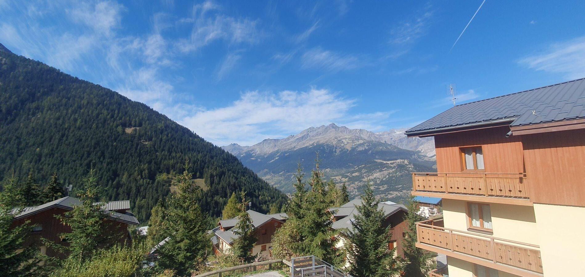 A mountain cabin with a balcony, surrounded by trees and a view of distant mountains.