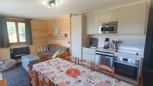 A cozy cabin interior with a wooden interior, a dining table with a checkered tablecloth, a sofa, a small TV, and a kitchenette with modern appliances. - 100m from ski slopes, 1st floor, balcony, ski locker, 48m², Valfréjus (Valfréjus)