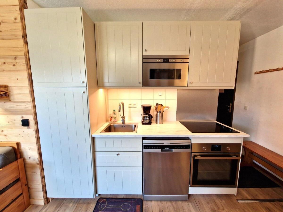 A compact kitchen with white cabinetry, a stainless steel dishwasher, a double oven, and a microwave.