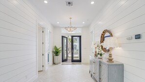 A hallway with white paneling, a herringbone floor, a chandelier, a mirror, and a cabinet with decorative items. - Elegant Beach House with views, pool, ping pong, shuffleboard - steps to beach (Port Aransas)