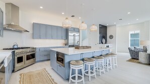 A modern kitchen with a central island, stainless steel appliances, and pendant lighting. - Elegant Beach House with views, pool, ping pong, shuffleboard - steps to beach (Port Aransas)
