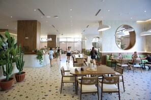 A spacious indoor dining area with wooden tables and chairs, potted plants, and a modern ceiling design.