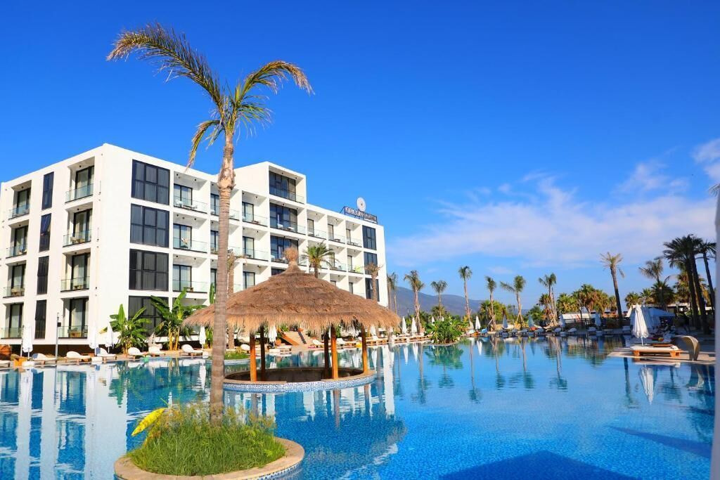 Un hôtel doté d’une grande piscine, de palmiers et d’une structure surmontée d’un toit de chaume.