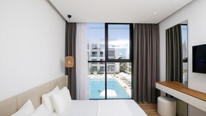 A hotel room with a large bed, a TV, a desk, and a view of a swimming pool. - Oricon Coast (Orikum)