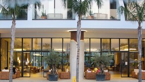 A modern hotel lobby with a pool, outdoor seating, and large windows. - Oricon Coast (Orikum)