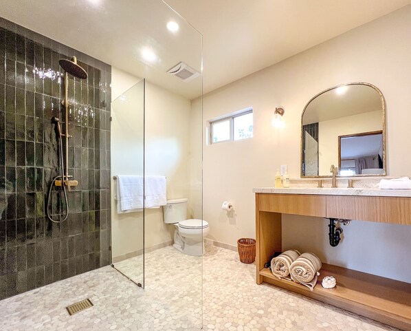 Une salle de bain moderne avec une douche à parois de verre, des toilettes, un lavabo avec un miroir et une étagère avec des serviettes.