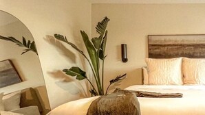 Hotellihuone, jossa on suuri sänky, yöpöytä, peili ja ruukkukasvi.