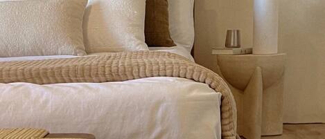 A neatly made bed with a wooden headboard, a bedside table with a vase of flowers, and a small wooden stool.