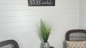 A room with two wicker chairs, a small table with a plant, and a sign that reads "STAY awhile". - New Holley Rentals studio apartment in Vicksburg (Vicksburg)