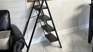 A loft-style bedroom with a bed, a black metal ladder, a black shelving unit, and a white wall with horizontal lines. - New Holley Rentals studio apartment in Vicksburg (Vicksburg)