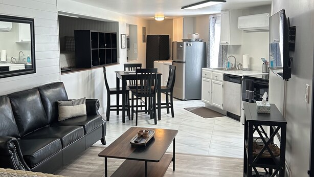 A modern living room with a black leather sofa, a wooden coffee table, and a dining area with a black table and chairs. There is a kitchen area with a refrigerator, sink, and cabinets. - New Holley Rentals studio apartment in Vicksburg (Vicksburg)