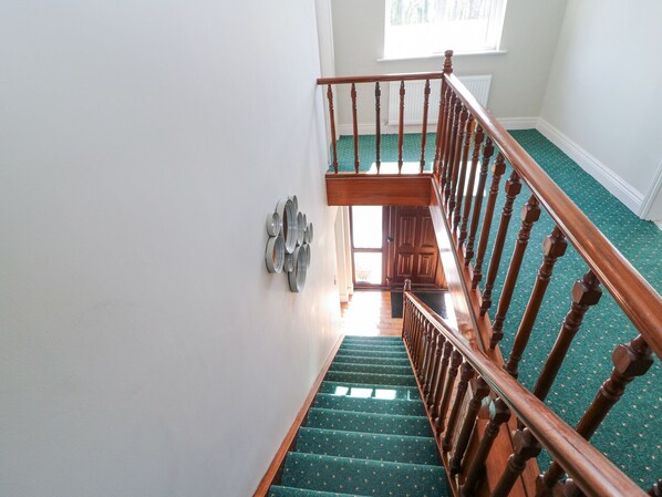 Un escalier avec des rampes en bois et des marches recouvertes d’une moquette verte, menant à un palier.