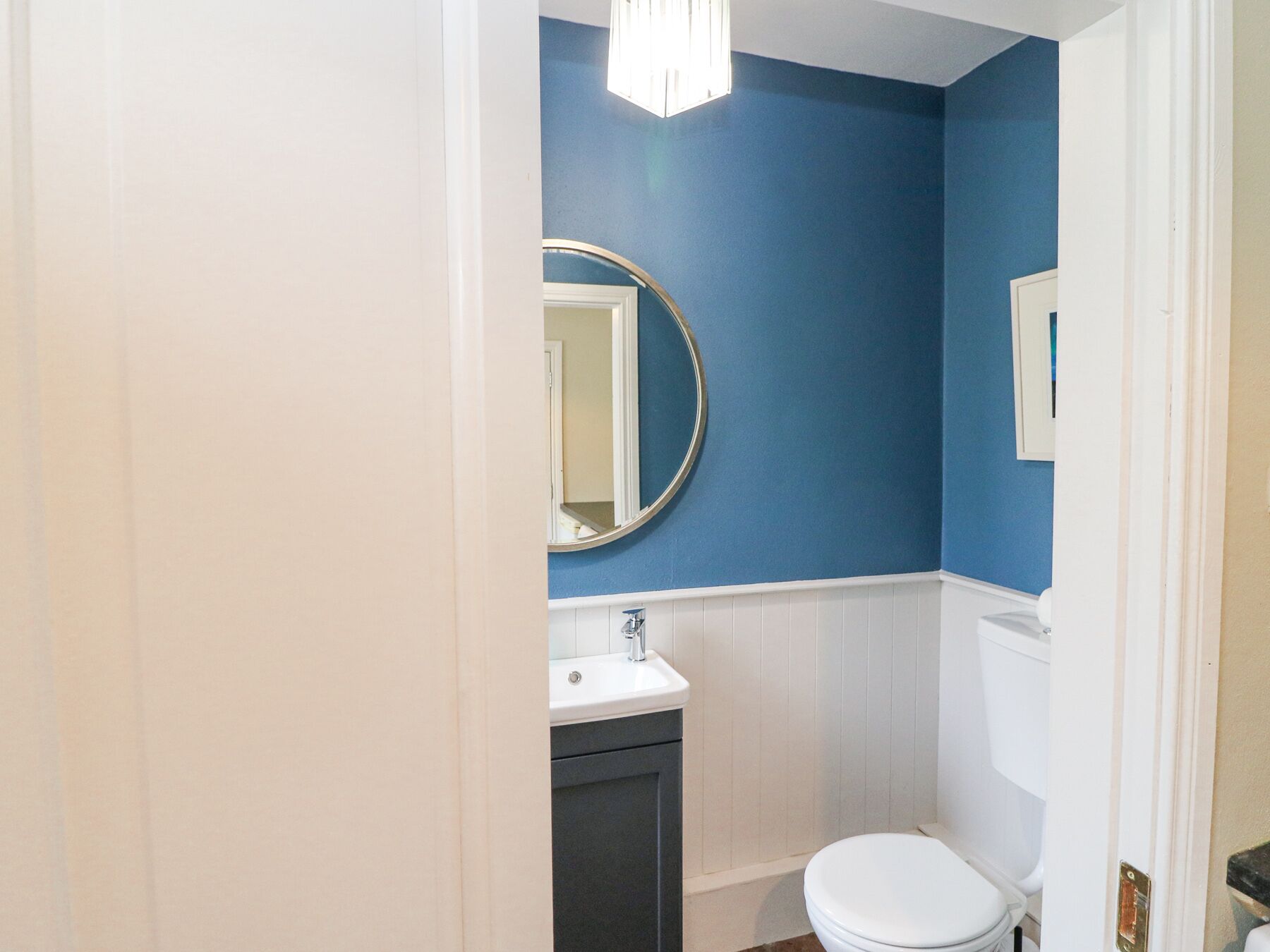 A bathroom with a white sink, a round mirror, a white toilet, and a blue wall.