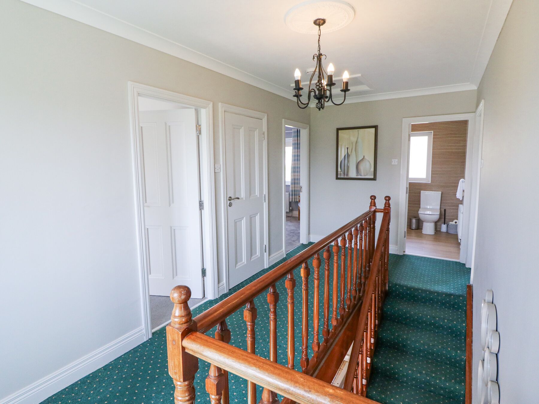 Ein Korridor mit einer Holztreppe, weißen Türen, einem Chandelier und einem gerahmten Bild an der Wand.