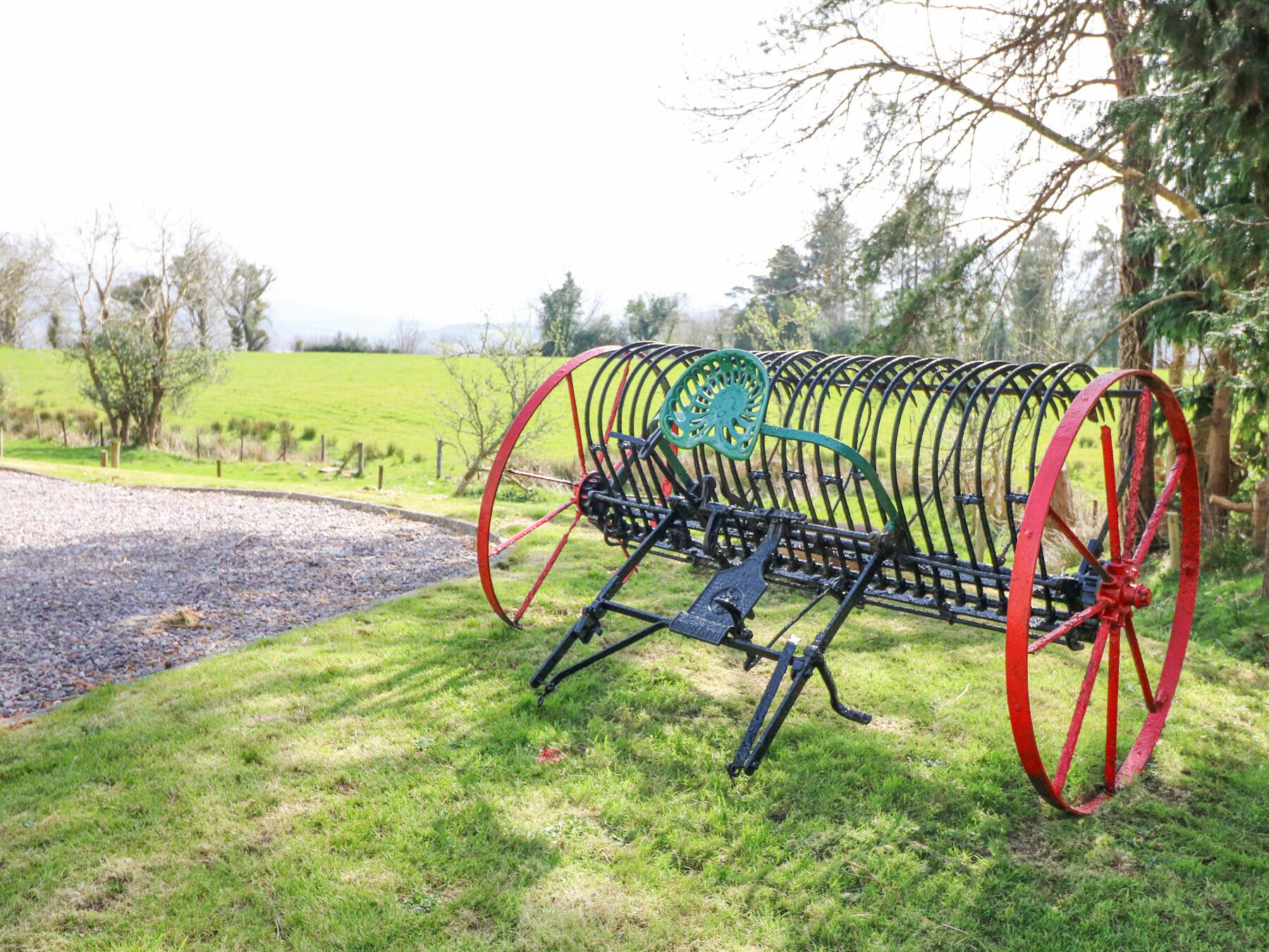 A stationary, open-frame, metal structure with red wheels, set on grass in a rural setting.