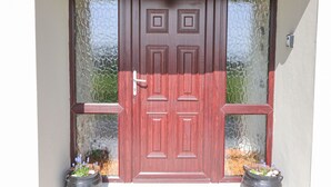 A red wooden door with a glass panel, flanked by two potted plants.
