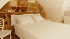 Quarto com cabeceira de pedra, cama branca e cadeira branca.