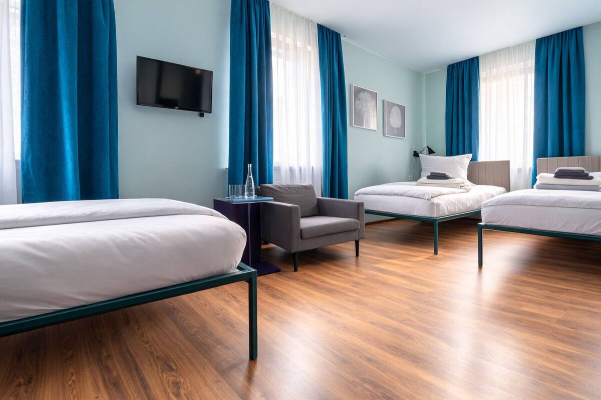 A hotel room with two single beds, a sofa, a chair, a TV, and a small table.