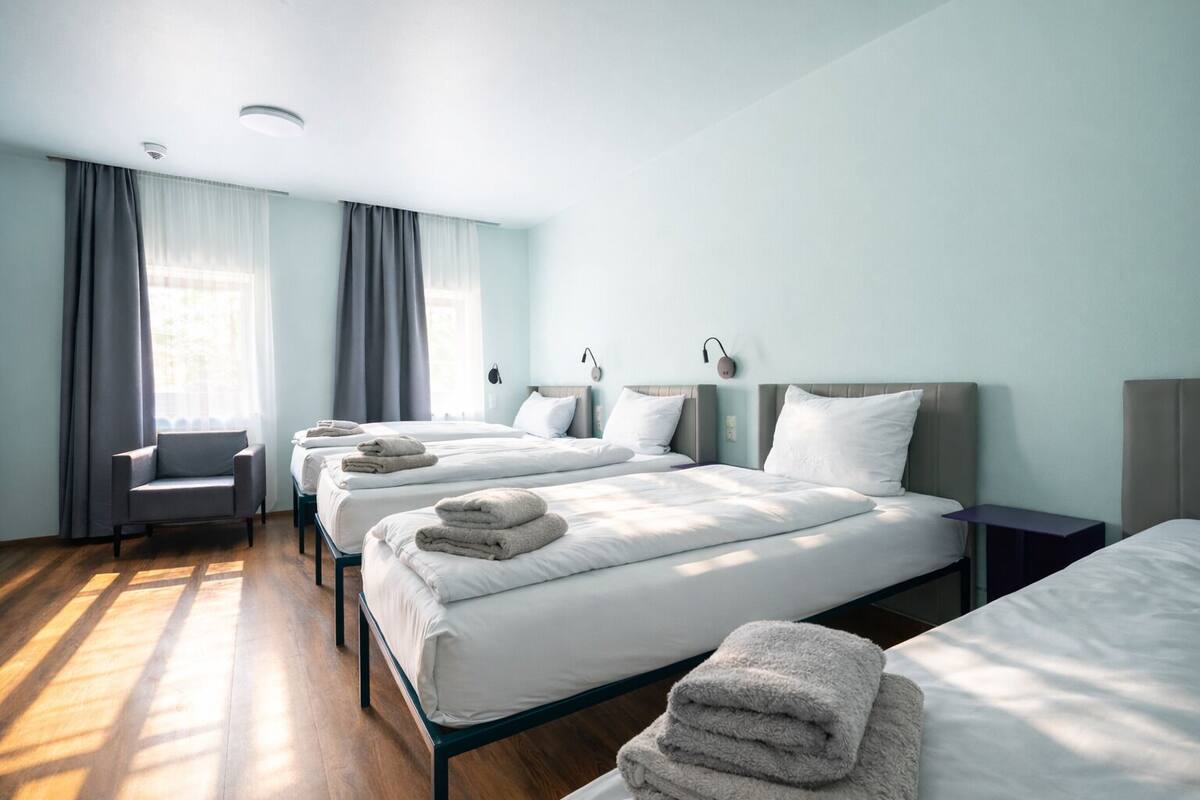 A hotel room with three beds, a chair, and a desk.