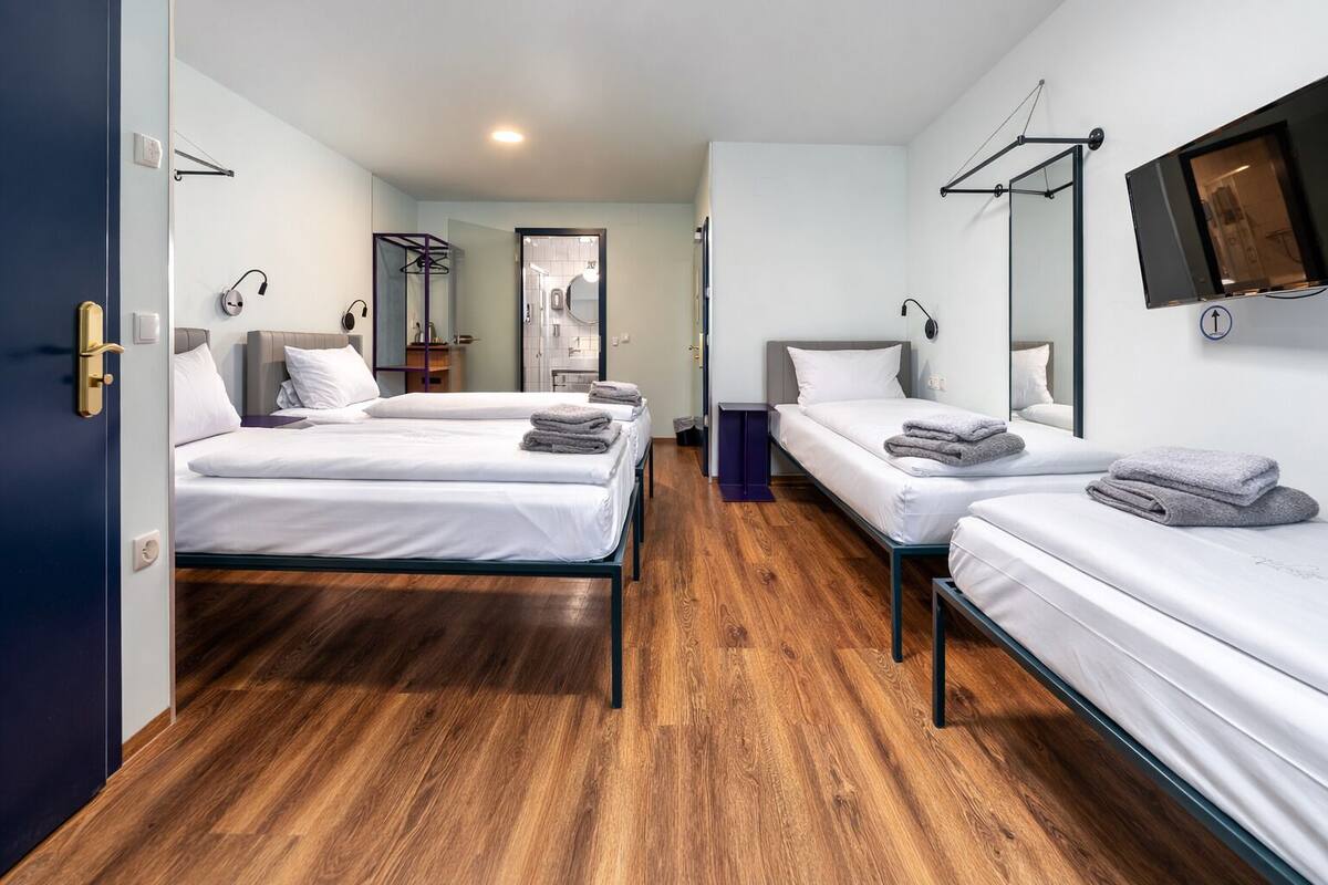 A hotel room with two single beds, a wooden floor, a TV mounted on the wall, and a mirror above the bed.