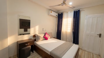 Un dormitorio con cama, mesita de noche, televisor, aire acondicionado y una puerta.