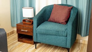 Un fauteuil de couleur turquoise avec un coussin à motifs rouges, une table de chevet en bois avec une lampe, et un plancher en bois.