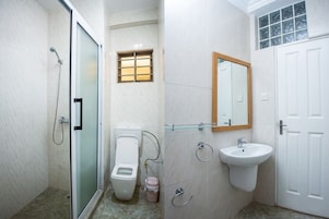 Un baño con cabina de ducha de vidrio, inodoro, lavamanos y espejo.
