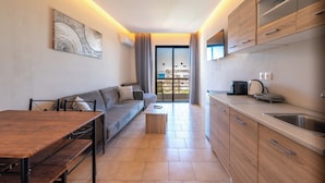 A modern kitchen with a dining area, wooden cabinets, a built-in oven, and a large window. - Blue Wave Suites - Ixia (Rhodes)