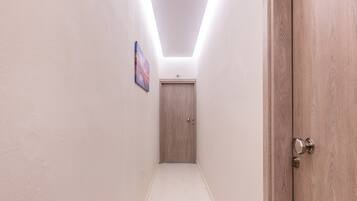 Un pasillo con una puerta de madera a la derecha, una puerta al fondo y un cuadro en la pared.