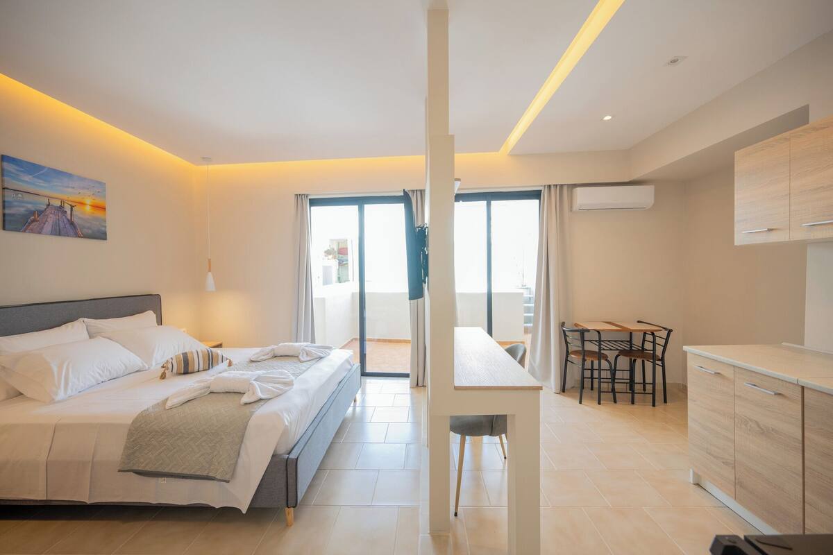 Habitació d'hotel moderna amb llit, zona de dinar i petita cuina.