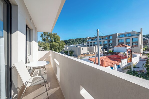 A balcony with a table and chairs, overlooking a residential area with modern buildings and a clear sky. - Blue Wave Suites - Ixia (Rhodes)