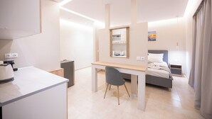 A modern hotel room with a desk, chair, bed, and a small kitchenette area. - Blue Wave Suites - Ixia (Rhodes)
