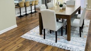 Een moderne keuken met witte kasten, roestvrijstalen apparatuur en een eethoek met een houten tafel en witte stoelen.